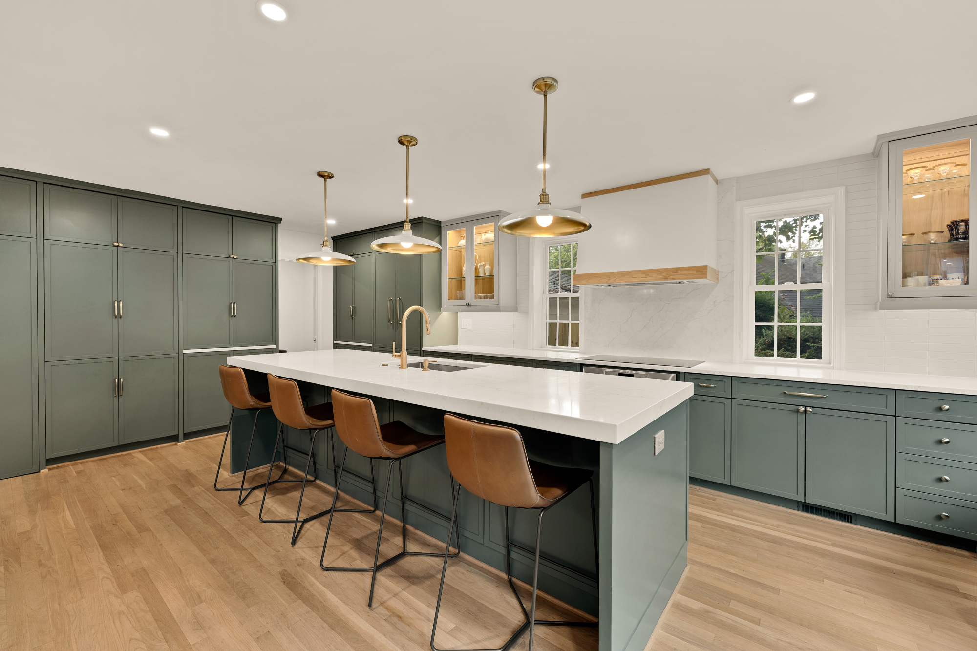 Spacious renovated kitchen with sage-green cabinets, oversized island and brass fixtures