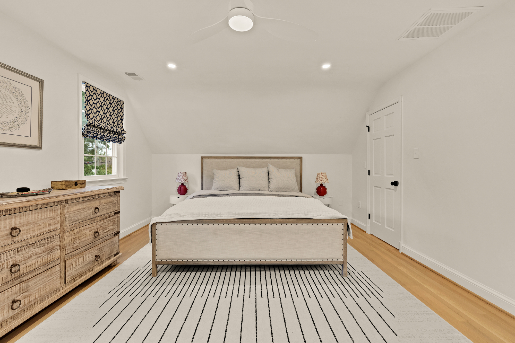 Renovated upstairs primary bedroom with vaulted ceiling and warm wood floors