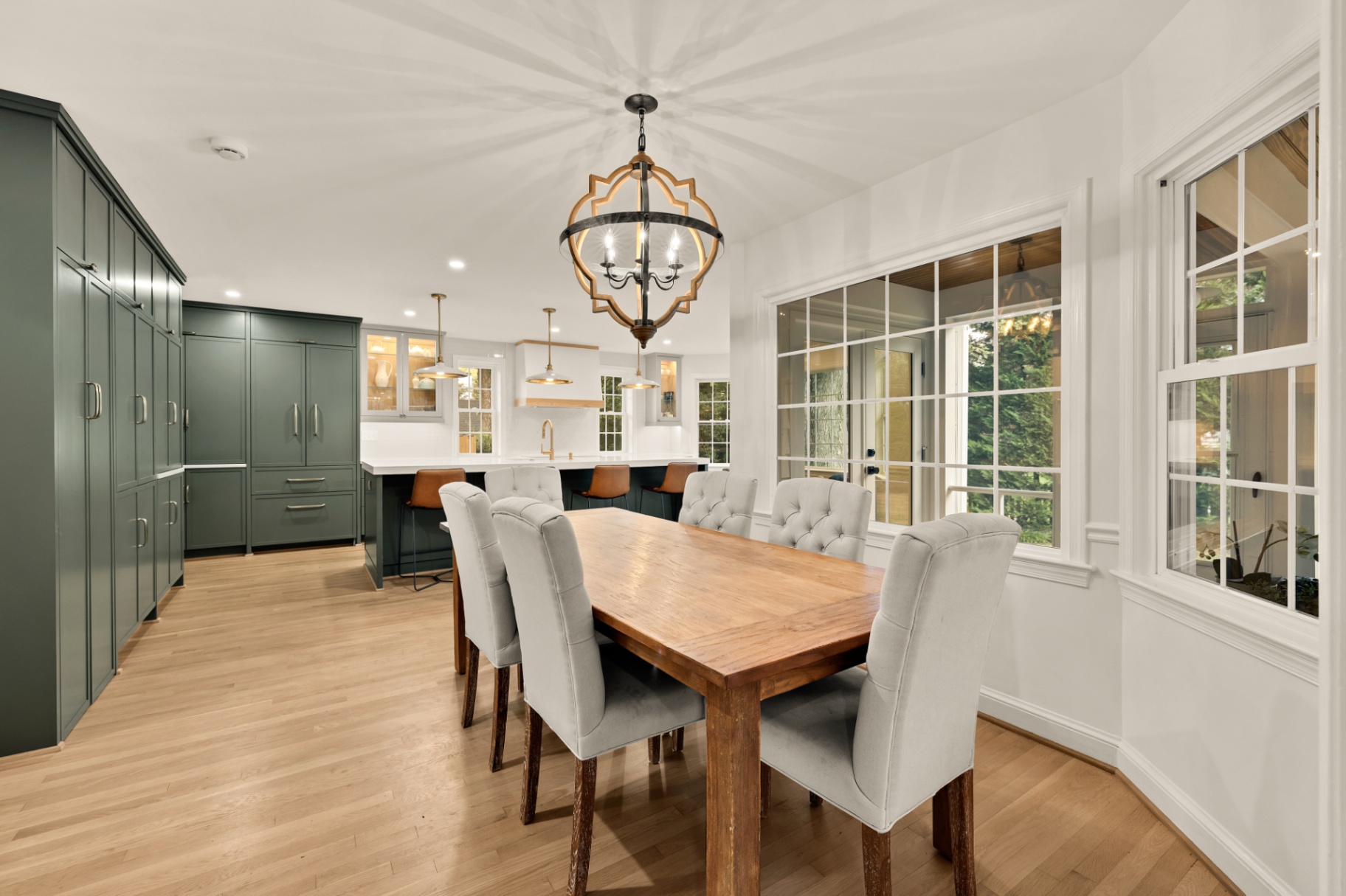 Open kitchen and dining area with custom green cabinetry and wood farmhouse table