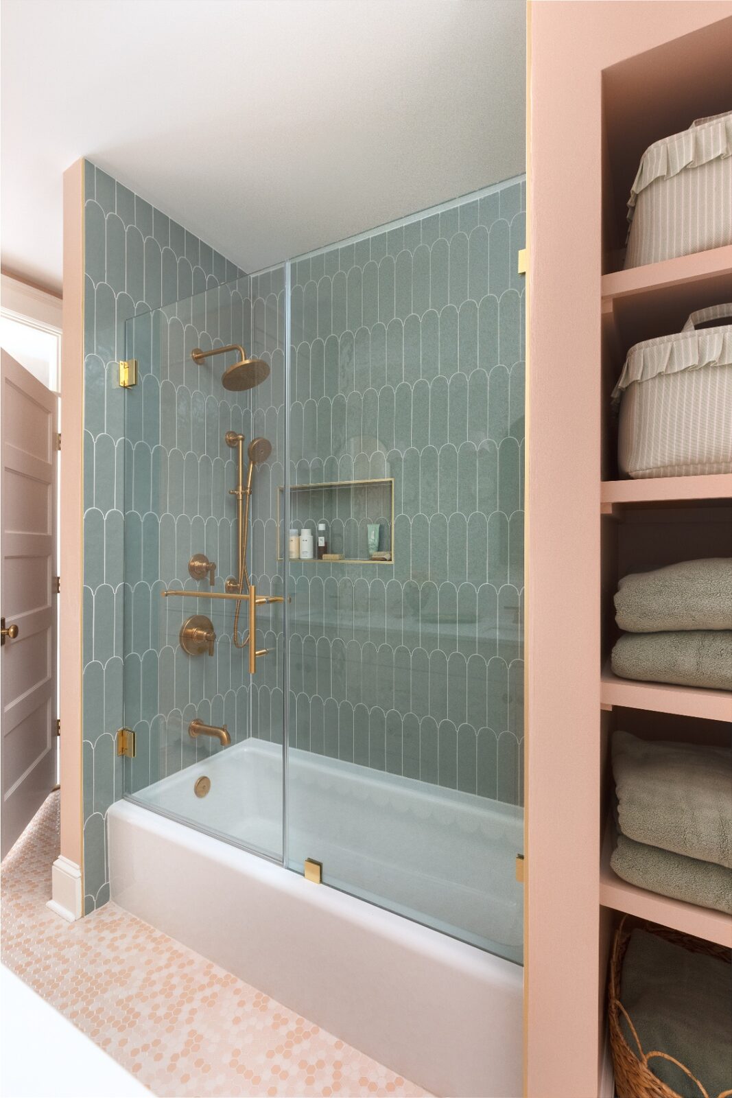 Sage-green fan-tile tub surround with brass fixtures and a built-in linen closet